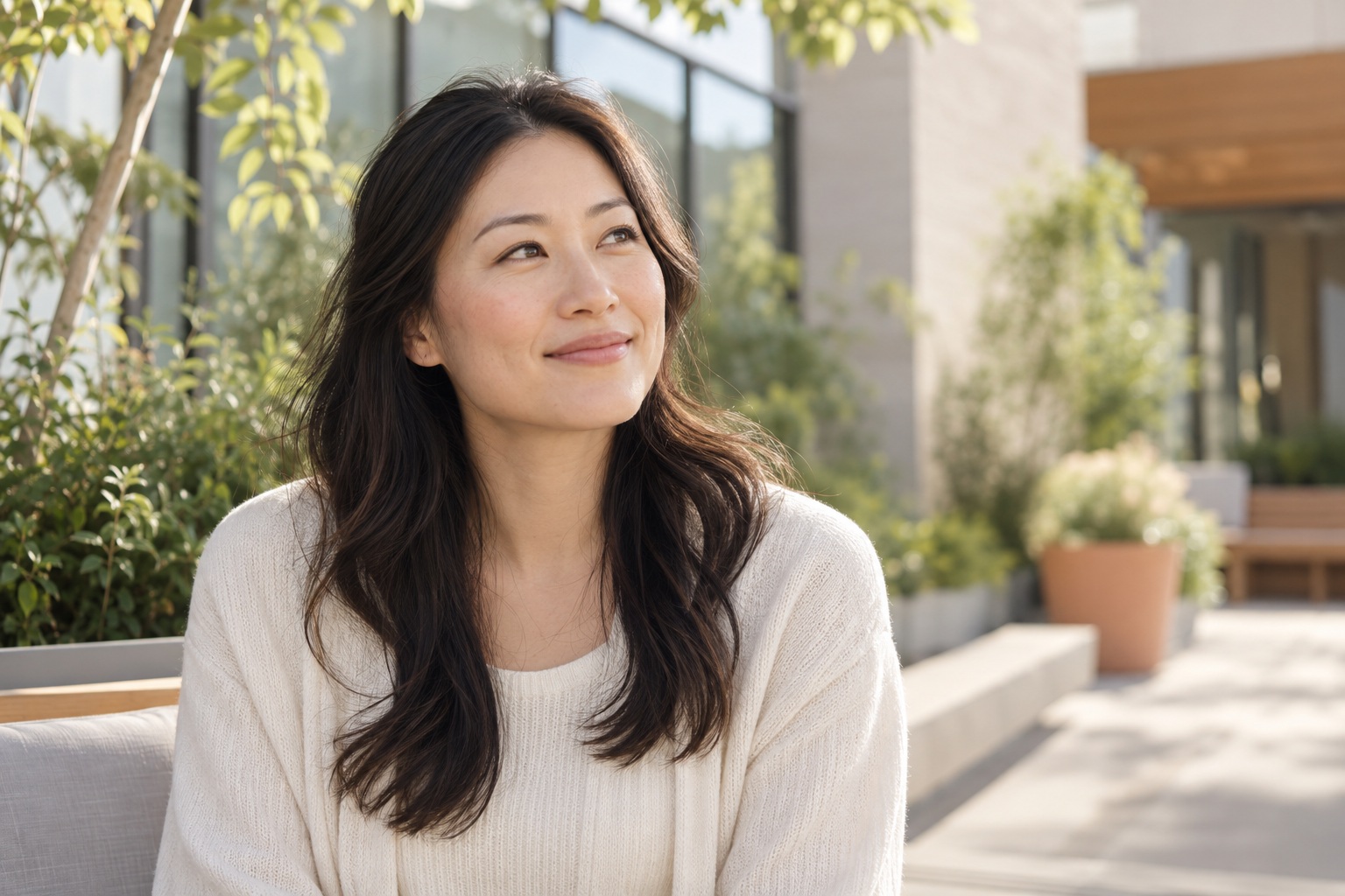 An East Asian woman smiling in a calm sunlit setting.